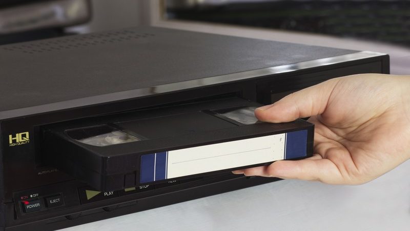 Personne rentrant une cassette VHS dans un lecteur de ce média